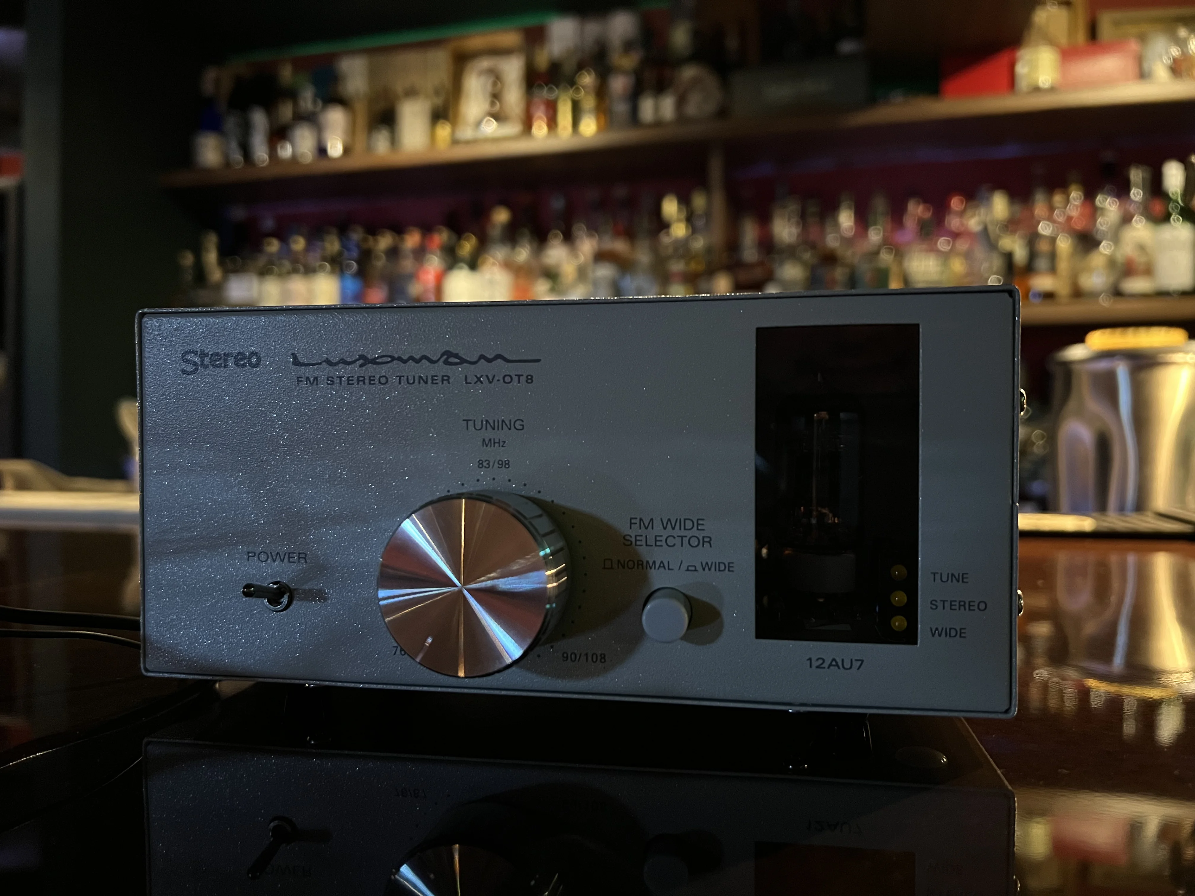 Inside the bar, a phone and menu rest on the wooden counter, with bottle shelves and brass-colored lighting in the back